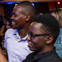 Two boys side by side, one hold champagne glass and the other holding phone.